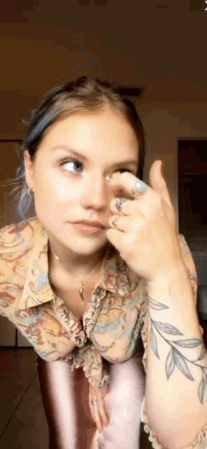 a woman with a tattoo on her arm is touching her face with her hand .
