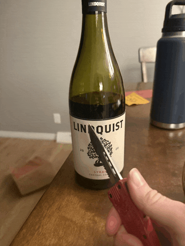 a bottle of linquist syrah is being cut with a knife