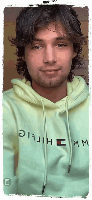 a man is wearing a green hoodie that says ' tommy hilfiger ' on it