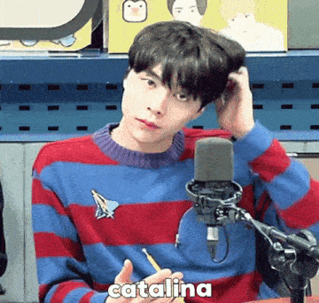 a young man in a striped sweater is sitting in front of a microphone and writing in a notebook .