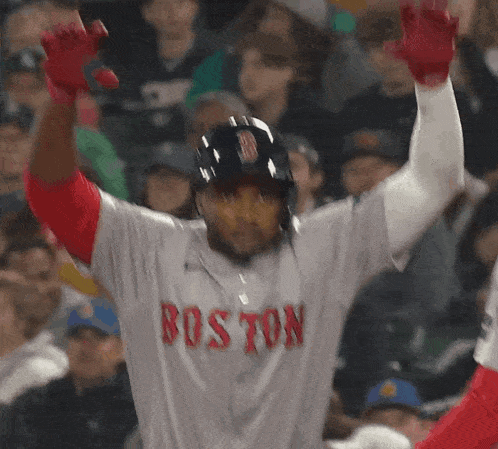 a baseball player wearing a boston jersey holds his arms up in the air