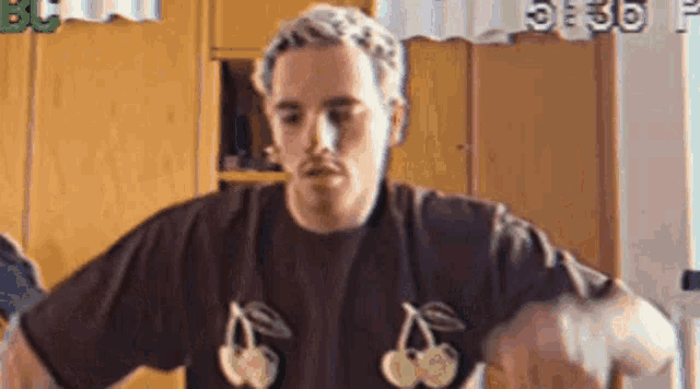 a man wearing a brown t-shirt with cherries on it is standing in front of a wooden wall .