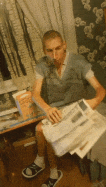 a man sitting on a bed reading a newspaper with a box of cheerios in the background