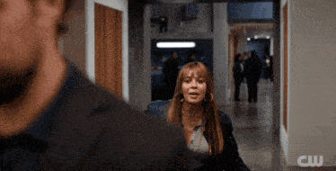 a woman is walking down a hallway with a cw logo behind her