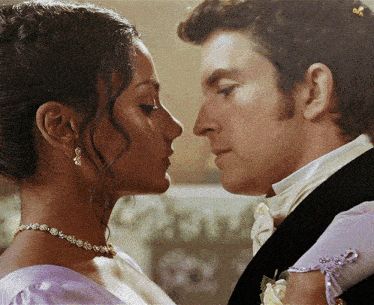 a man in a tuxedo and a woman in a purple dress look at each other