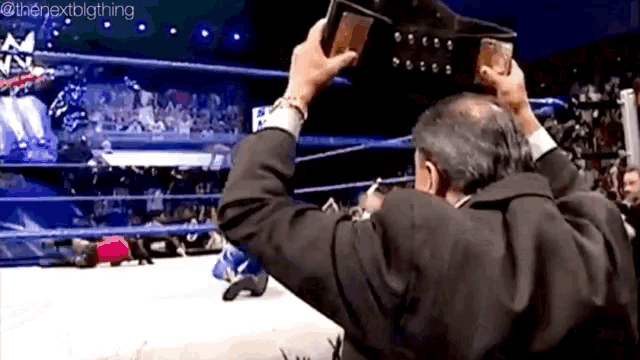 a man in a suit is holding a wrestling championship belt over his head .