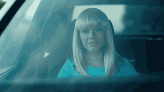 a blonde woman in a blue dress is sitting in a car