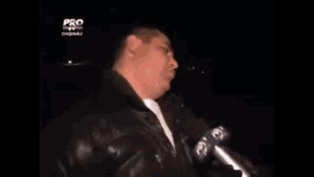 a man is talking into a microphone while wearing a black jacket .