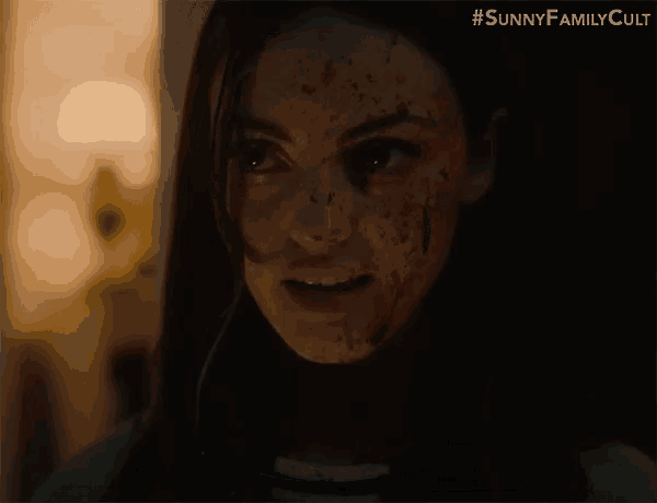 a close up of a woman with blood on her face in a dark room .