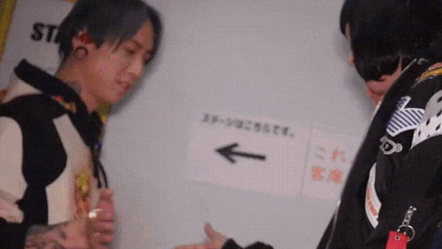 two men are standing next to each other in front of a sign with an arrow pointing to the left