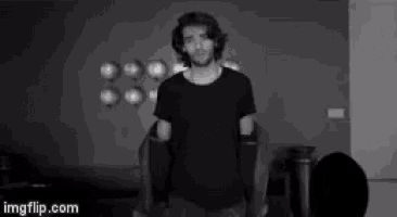 a man in a black t-shirt is standing in a room with balloons on the wall .