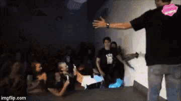 a man in a black shirt is standing in front of a group of people in a dark room .