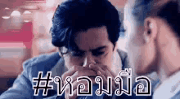 a man is covering his mouth with his hands while a woman looks at him .