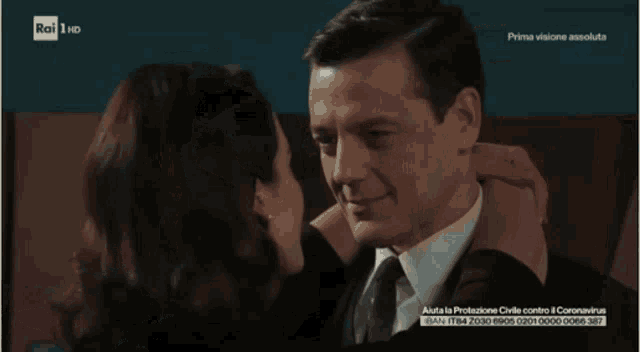 a tv screen shows a man and woman hugging with the words prima visione assoluta at the top