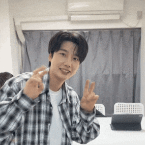 a young man wearing a plaid shirt is giving a peace sign