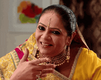 a woman wearing a yellow top and gold jewelry is smiling and giving a thumbs up