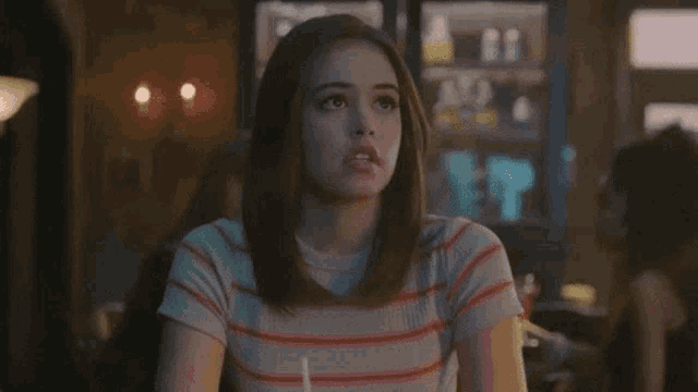 a young woman in a striped shirt is sitting at a table in a restaurant .