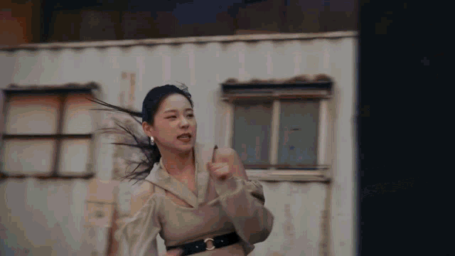 a young woman is running in front of a building with her hair blowing in the wind