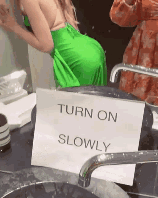 a woman in a green dress is standing in front of a mirror with a sign that says turn on slowly