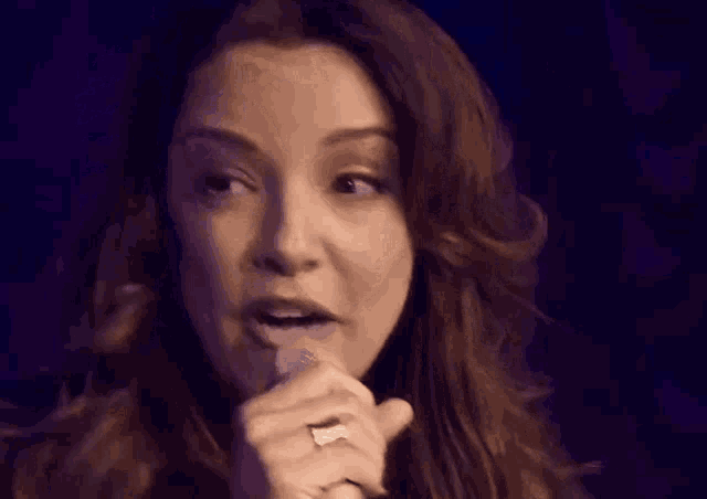 a woman singing into a microphone with a dark background
