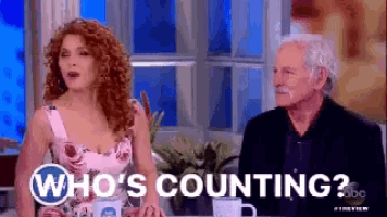 a man and a woman are sitting at a table with the words who 's counting written on the screen .