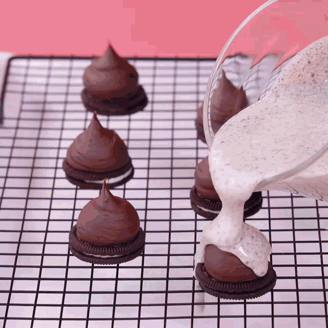 a person pouring frosting on oreos on a wire rack