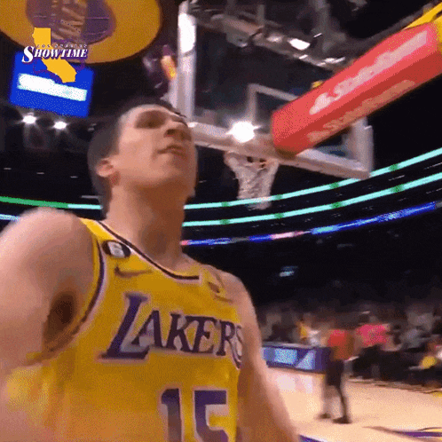 a basketball player wearing a lakers jersey looks up at the basketball hoop