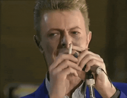 a man in a blue jacket is singing into a microphone and smoking a cigarette