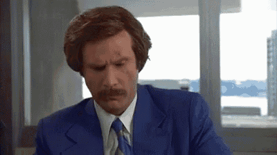 a man with a mustache and a blue suit is sitting at a desk .