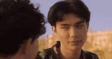 two young men are looking at each other and one of them is wearing a hawaiian shirt .