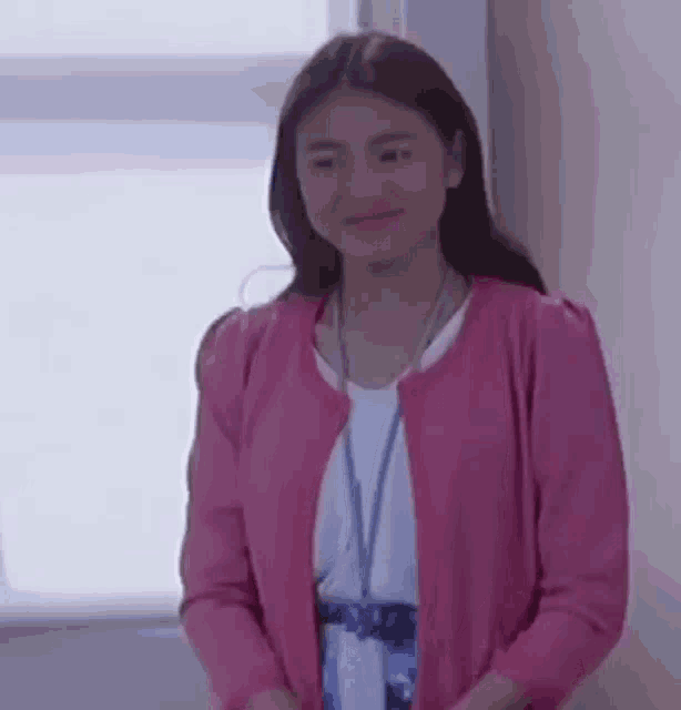 a woman is wearing a pink cardigan and a lanyard around her neck .