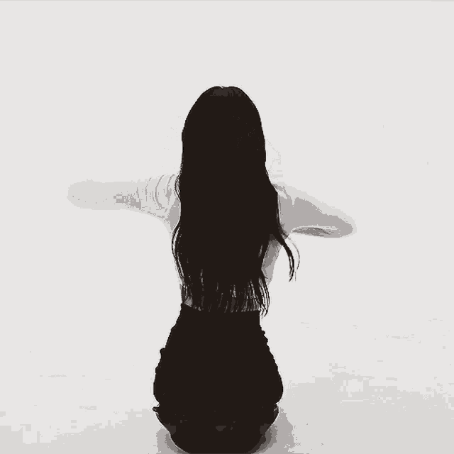a black and white photo of a woman kneeling with her hair blowing in the wind
