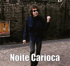 a man is dancing in front of a brick wall and the caption noite carioca