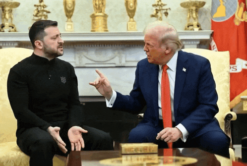 two men are sitting on a couch and one of them is wearing a black shirt with a ukrainian flag on it