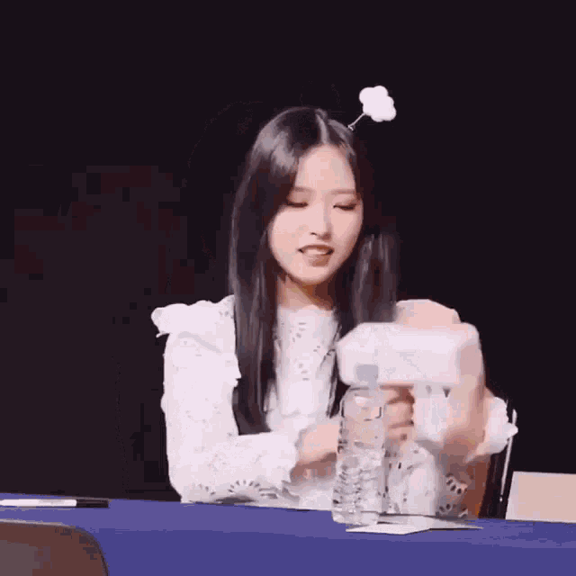 a girl is sitting at a table holding a bottle of water and a tissue .