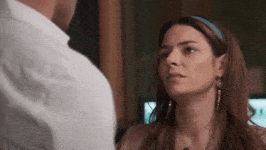 a man and a woman are looking at each other in a room . the woman is wearing earrings and a headband .