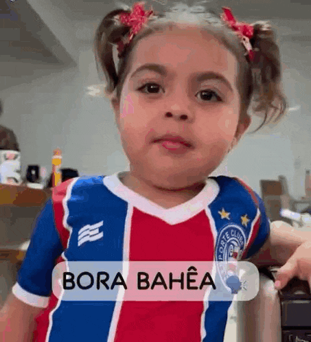 a little girl is wearing a red , white and blue soccer jersey and making a funny face .