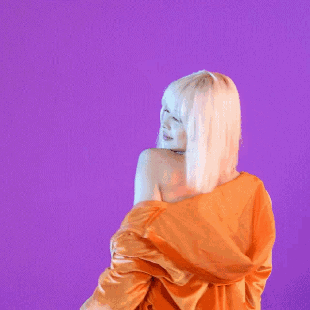 a woman in an orange jacket is standing in front of a purple backdrop