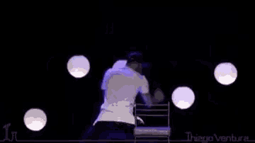 a man in a white shirt is sitting in a chair on a stage in front of purple lights .