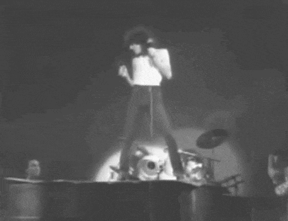 a black and white photo of a man singing into a microphone on stage .