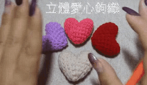 a person with purple nails is holding a crocheted heart in their hand .