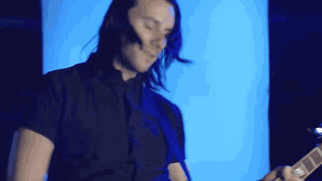 a man in a black shirt and tie is playing a guitar in front of a blue light .
