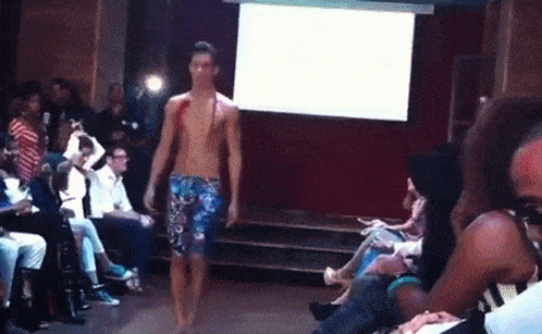 a model walks down the runway at a fashion show in front of a projector screen