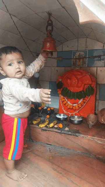 a baby is holding a bell in front of a red statue