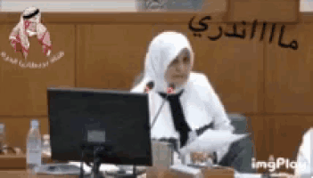 a woman in a hijab is sitting in front of a microphone in front of a computer .