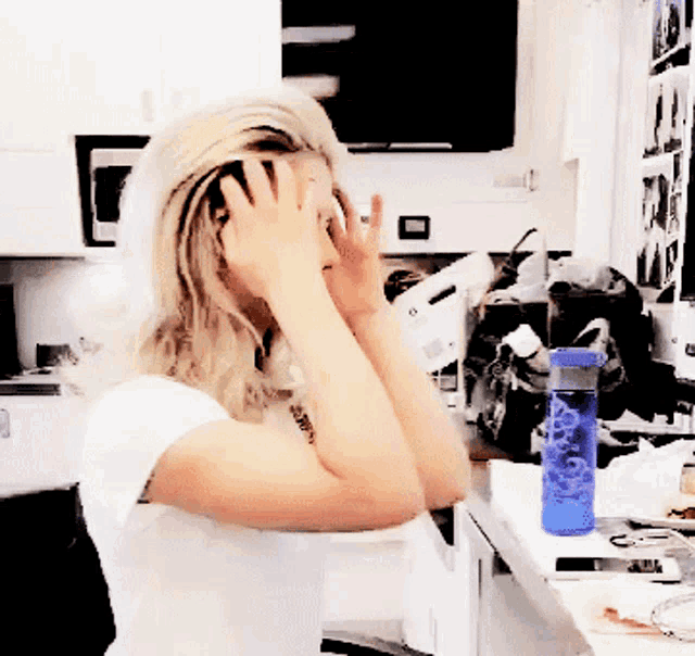 a woman covering her face with her hands while a blue water bottle sits on a counter
