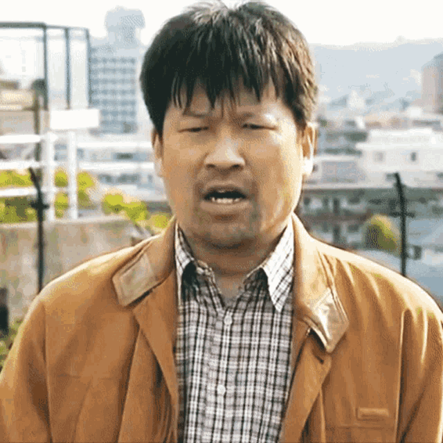 a man wearing a plaid shirt and a brown jacket is making a face