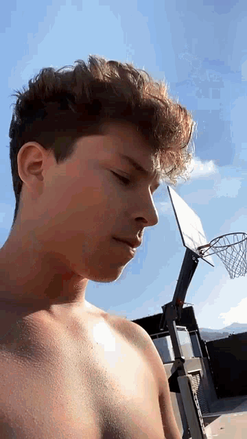 a shirtless young man stands in front of a basketball hoop