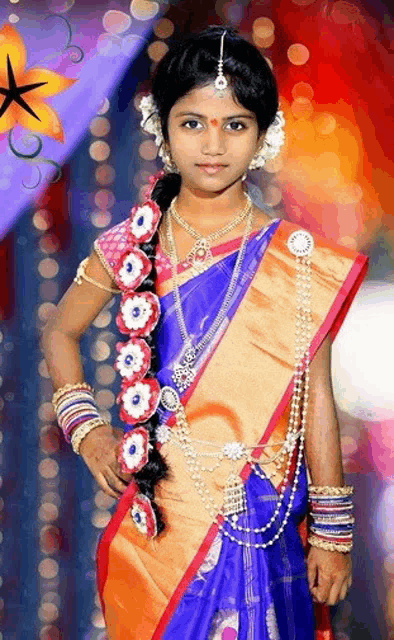 a little girl in a blue and gold saree is wearing a lot of jewelry .
