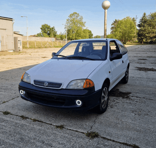 a white suzuki car is parked on a concrete surface